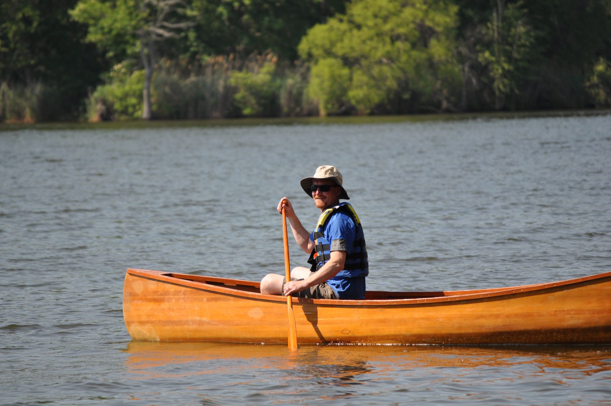 candidate Joe Jasper paddles a wooden canoe on pond.