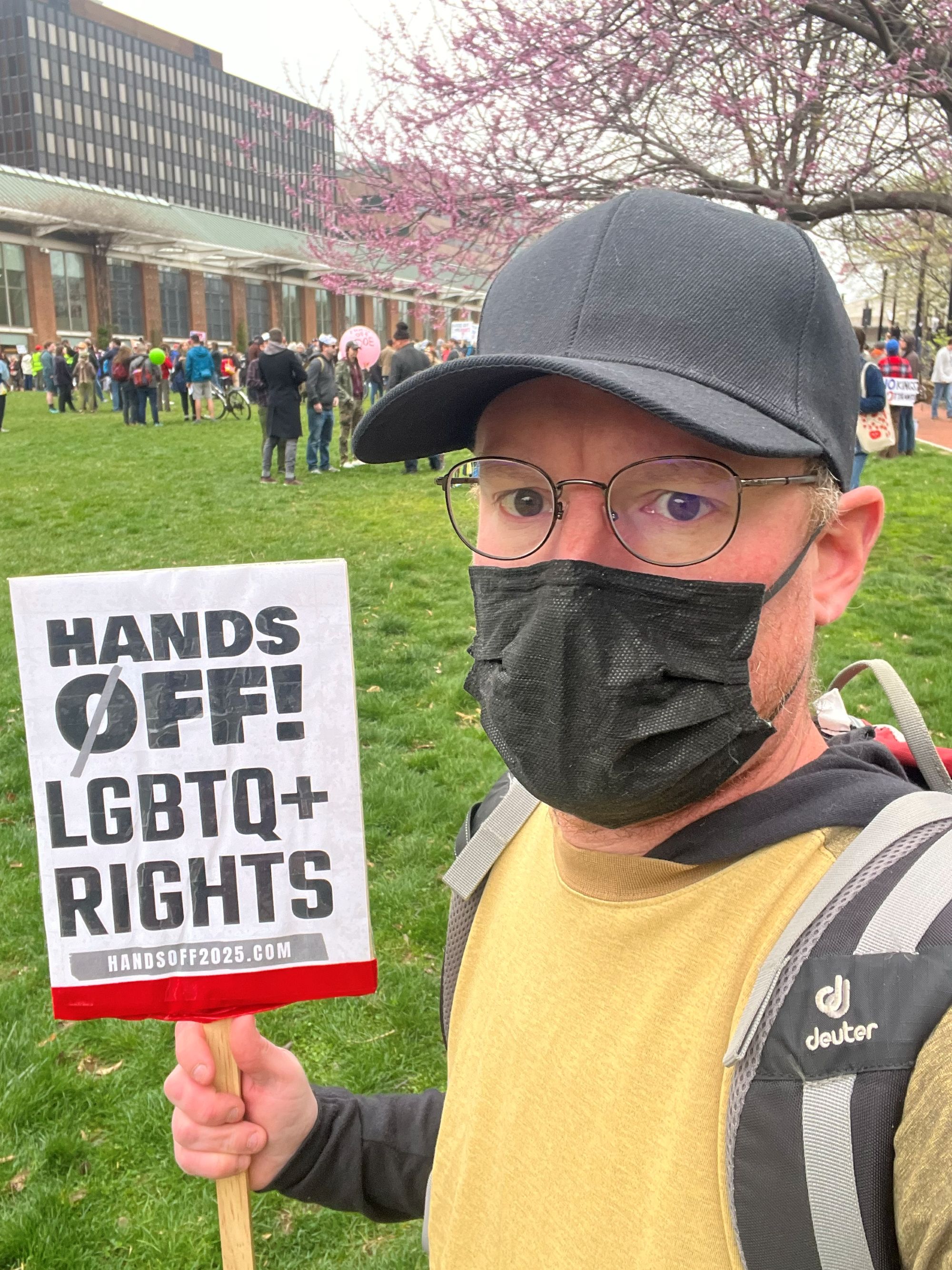 candidate Joe Jasper stands with a sign at a protest. the sign reads: Hands off LGBTQ+ rights!