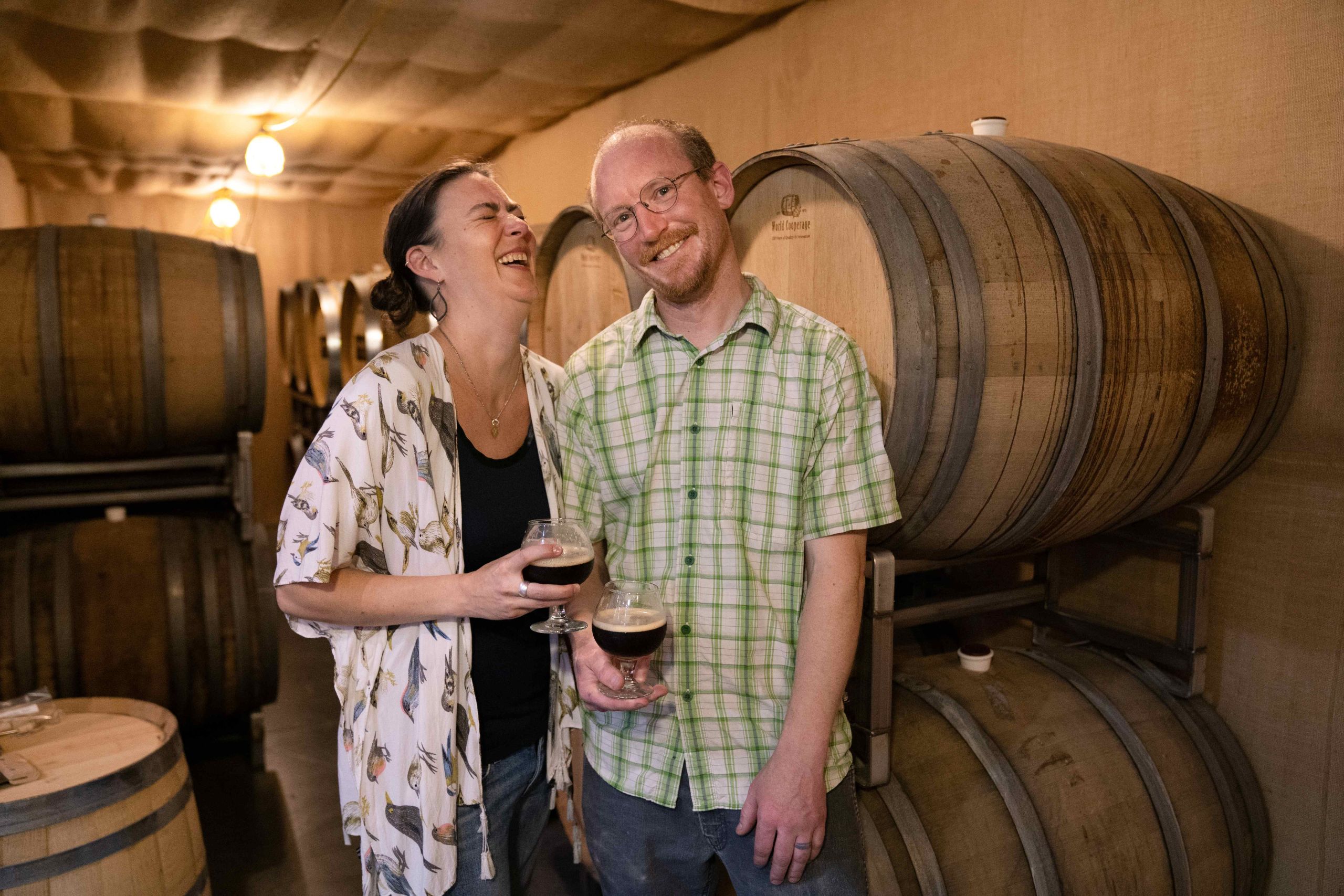 man and woman in barrel cave holding beers and laughing.
